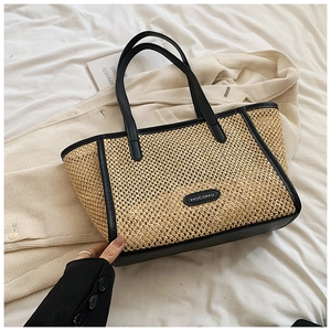 Détail du sac cabas en paille tressée avec anses en cuir noir sur fond neutre minimaliste