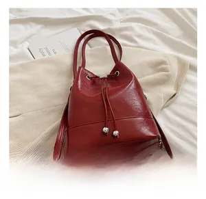 Dettaglio borsa a secchiello in pelle rossa con chiusura a coulisse e ciondolo a sfera