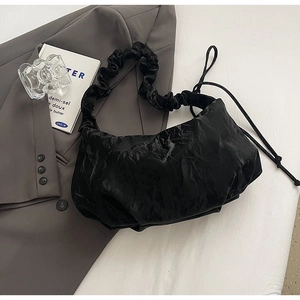 Detail of black pleated shoulder bag featuring scrunchie strap and wavy nylon texture