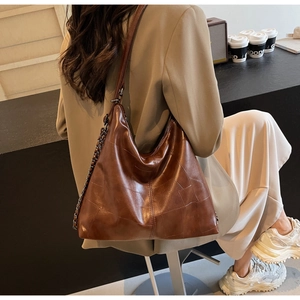 Detail of vintage dark brown leather tote bag with patchwork texture and chain accents