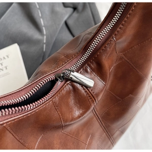 Macro detail of brown leather bag showing geometric patchwork and silver zipper