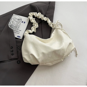 Detail of cream pleated cloud bag with marble texture and ruffled handle on grey blazer