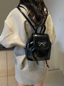 Mini black glossy patent leather backpack with silver metal bow on model back view