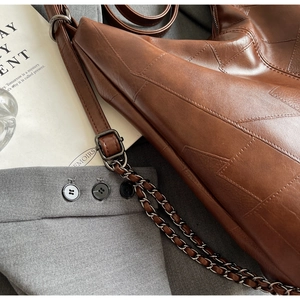 Macro detail of dark brown patchwork leather tote with vintage metal chain strap texture