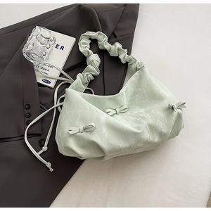 Detail of mint green pleated shoulder bag with scrunchie strap and bow on grey suit