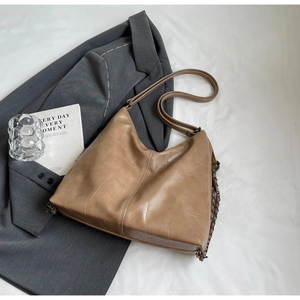 Macro detail of tan textured leather tote bag with dark metal chain decoration