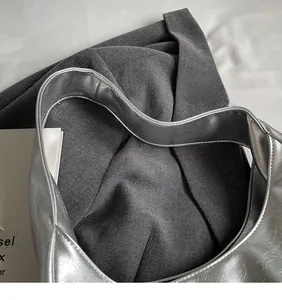 Detail of silver metallic tote bag featuring wrinkled texture and wide shoulder strap
