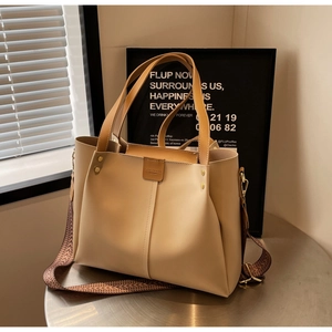 Dettaglio della borsa tote beige con ampia tracolla a motivi ondulati e inserti dorati