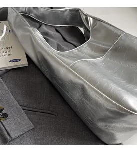 Detailed close-up of metallic silver tote bag with crinkled texture on grey blazer jacket