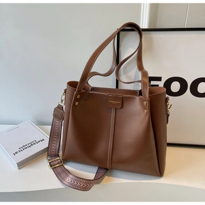 Dettaglio della borsa tote in pelle marrone con ampia tracolla intrecciata e logo dorato