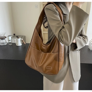 Detail of a brown tote bag featuring white contrast stitching and a fashion brand label