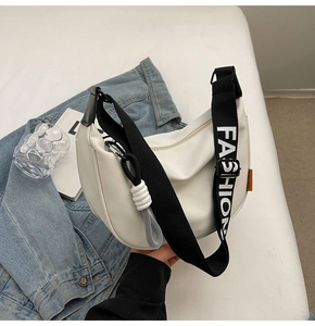 Detailansicht der weißen Halbmondtasche mit schwarzem FASHION-Gurt und Anhänger