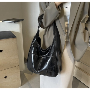 Detail of glossy black PU leather tote bag featuring contrast stitching and fashion tag