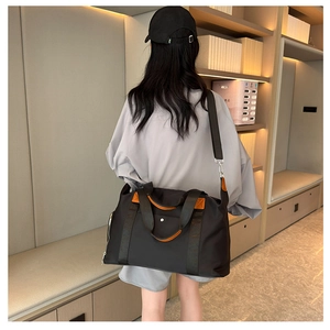 Large black Oxford travel bag with orange handles worn by model in a modern corridor