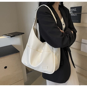 Detail of cream glossy hobo bag with front pocket and fashion label on black blazer