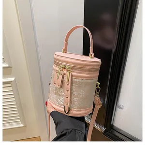 Detail of pink cylindrical bucket bag with floral lace pattern and gold hardware accents