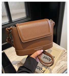 Detail of brown faux leather shoulder bag featuring vertical embossed texture and knotted strap