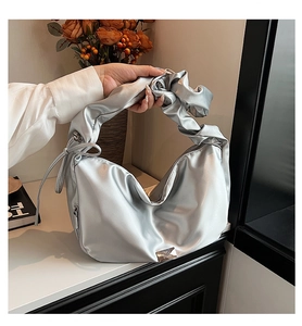 Macro detail of silver satin pleated bag with sleek ribbon bow and metal logo plate