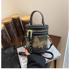 Detail of black cylindrical bucket bag featuring gold butterfly embroidery and metal studs