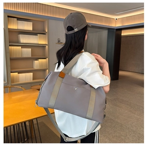 Modern grey nylon travel bag with brown leather accents held by a model in a library