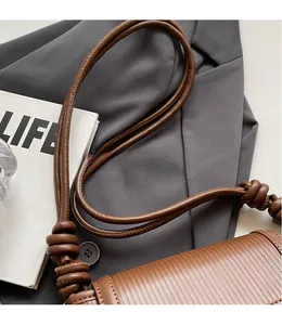 Detail of brown striped leather shoulder bag with decorative knot on long strap