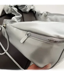 Detail view of the smooth silver zipper and pleated satin fabric on the shoulder bag