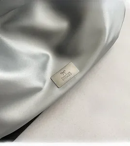 Close-up of Pantor Stories brushed metal logo plate on silver PU leather handbag