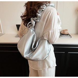 Sac bandoulière argenté en similicuir plissé porté par un mannequin dans un bureau