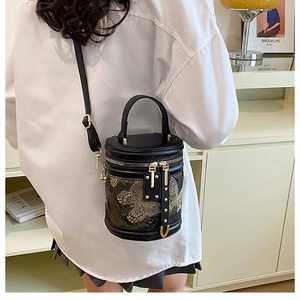 Detail of black cylinder bucket bag featuring intricate gold butterfly embroidery