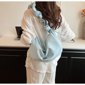 Detail of light blue hobo bag with pleated shoulder strap and metal logo on a model
