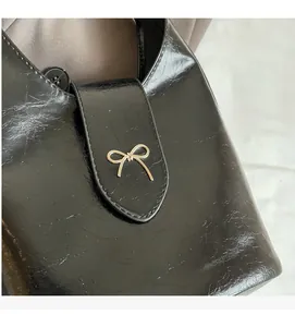 Detail of black crackle-texture bucket bag featuring a gold bow metallic buckle