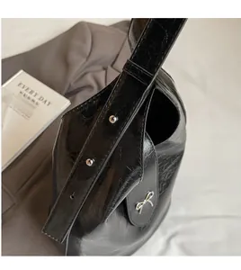 Detail of black glossy wrinkled shoulder bag with silver studs and bow metallic buckle