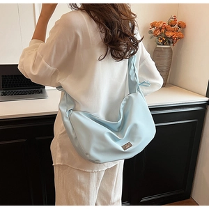 Vue détaillée du sac croissant bleu clair avec logo métallique et bandoulière de style urbain