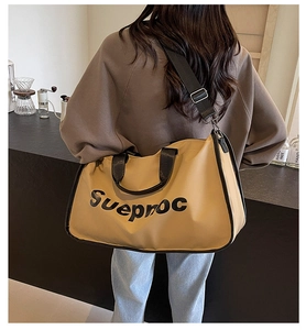 Detail of large ginger yellow travel tote bag with black handles and Sueproc letter print