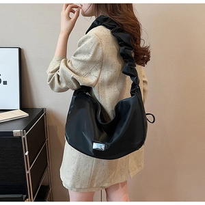 Détail de la bandoulière plissée noire sur grand sac croissant avec plaque logo argentée