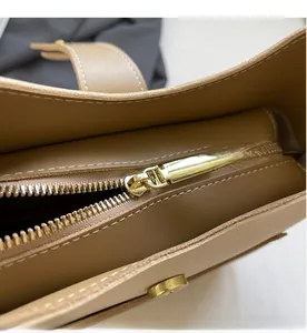 Close-up of golden zipper and magnetic buckle on khaki leather bucket bag with white stitching