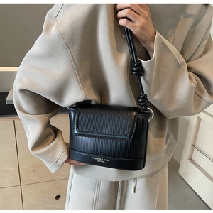 Detail of black crossbody bag with vertical stripe texture and knotted strap on a model