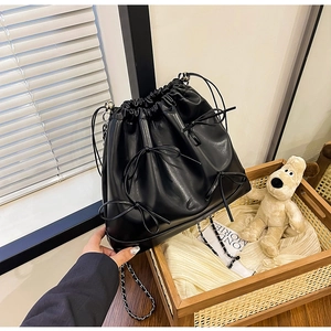 Dettaglio borsa a secchiello nera con coulisse, tracolla a catena e fiocchi decorativi