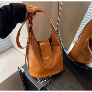 Detail view of brown leather bucket bag with silver metal bow and wide shoulder strap
