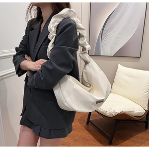 Close-up of beige dumpling bag featuring a unique ruched shoulder strap and metal plate
