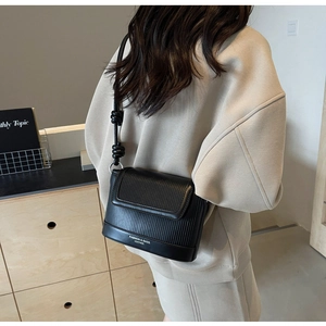Side view of a black vertical striped leather crossbody bag with knot shoulder strap