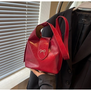 Detailed macro view of glossy red leather bucket bag with silver bow accent
