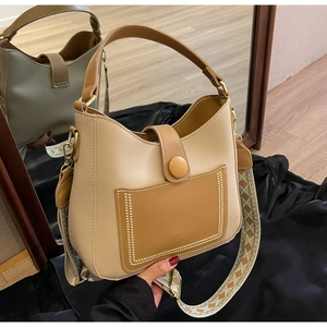 Detail of a two-tone leather bucket bag featuring a wide geometric ethnic strap and magnetic clasp