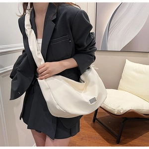 Sac croissant blanc moderne porté par un modèle, avec large bandoulière et texture en cuir mat