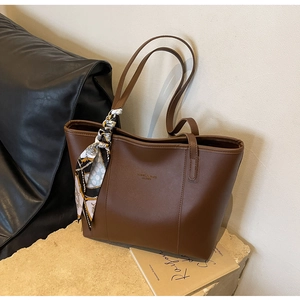 Detail of brown leather tote bag featuring fashion logo and geometric silk scarf decoration