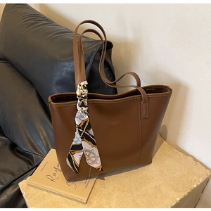 Detail of brown leather tote bag with decorative printed scarf on the handle