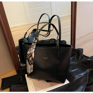 Detail of black leather tote bag with gold logo text and patterned decorative scarf