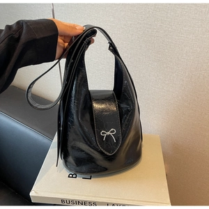 Detail of a black glossy bucket bag with pleated texture and a silver bow ornament