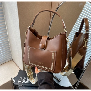 Close-up of brown bucket bag showing white stitching detail and wide patterned strap