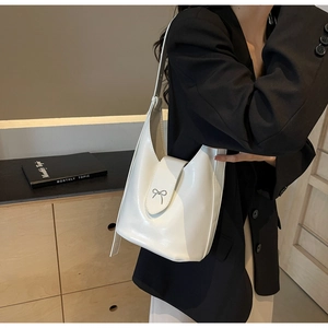 White faux leather bucket bag with silver bow hardware shown on a model's shoulder